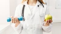Young dietitian with apple and dumbbell at clinic
