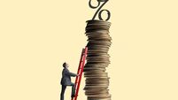 iStock-1323554443 (1).jpg Man Leans Ladder Against Tall Stack Of Coins Topped With Interest Rate Symbol