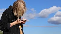 Teen girl playing online games by a smartphone on blue sky background. The concept of teenage addiction to a mobile phone and so