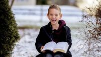 Sun rising over a cute little boy reading the Bible in the middle of a winter park