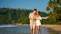 iStock-2196413825.jpg Romantic couple on beach holiday stroll hand in hand, sipping fresh coconuts. Laughing, chatting, they enjoy golden sunset. Perf